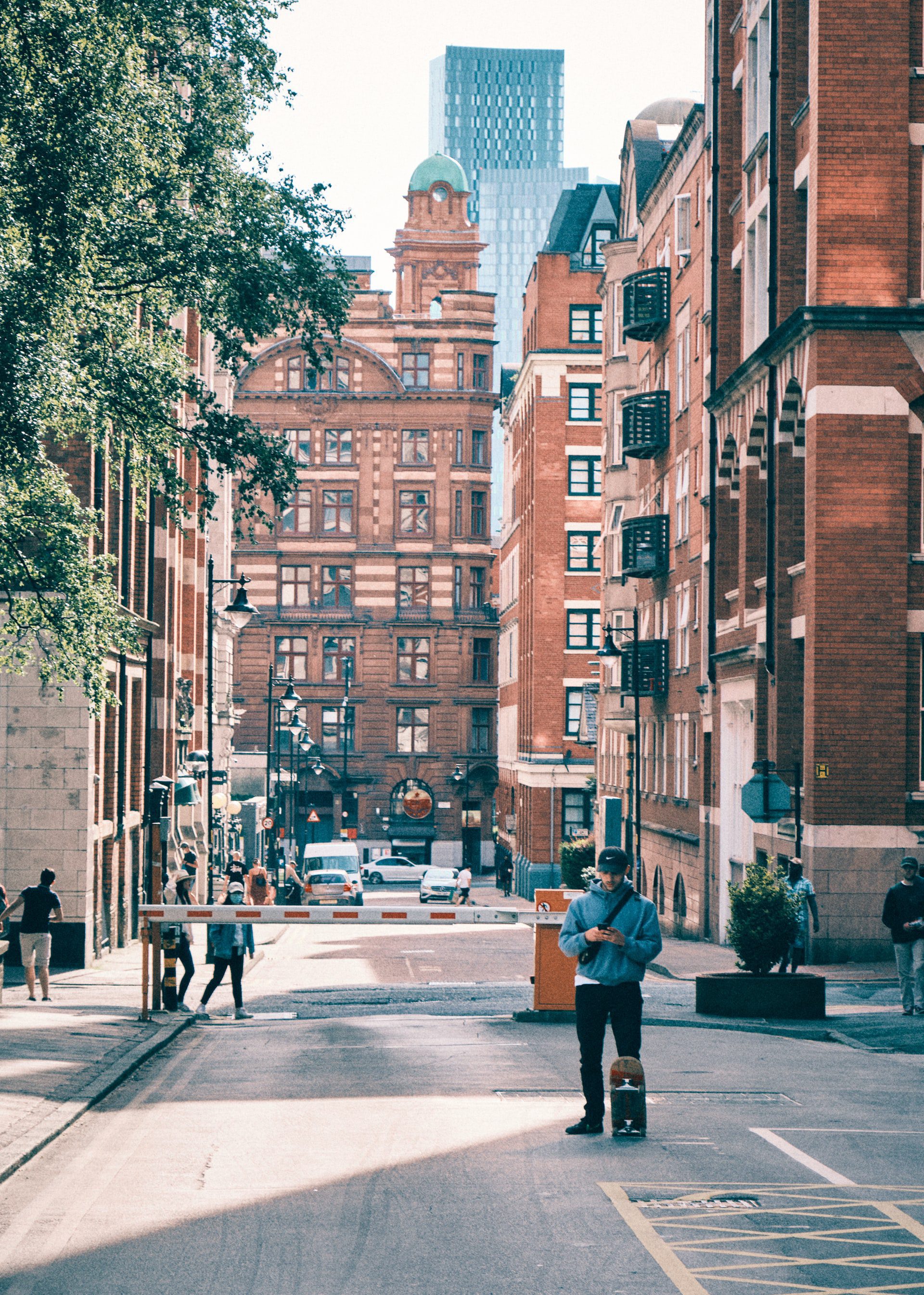 Boy texting and holding his skateboard in the streets of Manchester